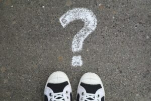 Sneakers on pavement with a chalk question mark, symbolizing curiosity or decisions.