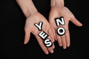 Two hands holding black and white letters spelling 'YES' and 'NO' on a black background.